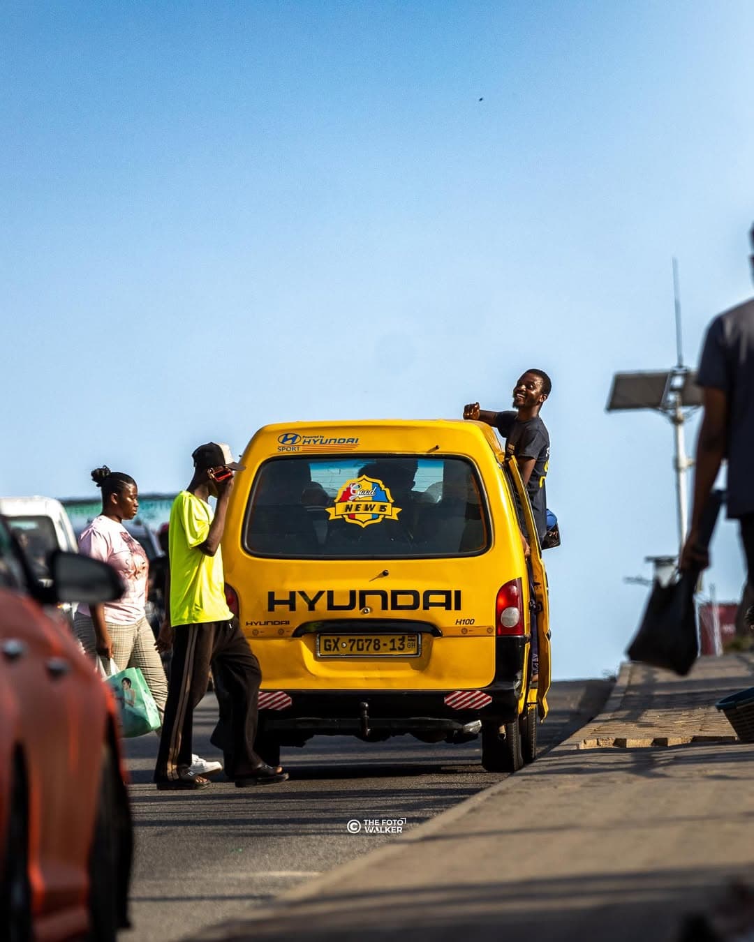 A trotro mate leaning out of a yellow trotro in Accra traffic